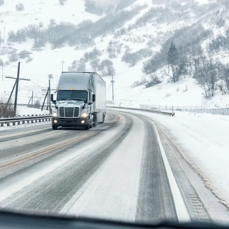 Semi-truck driving on a snowy mountain road through icy conditions